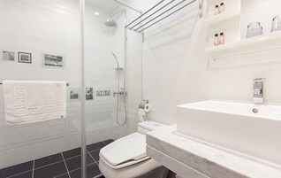 Un baño moderno con ducha envuelta en vidrio, inodoro blanco y lavabo de mármol.