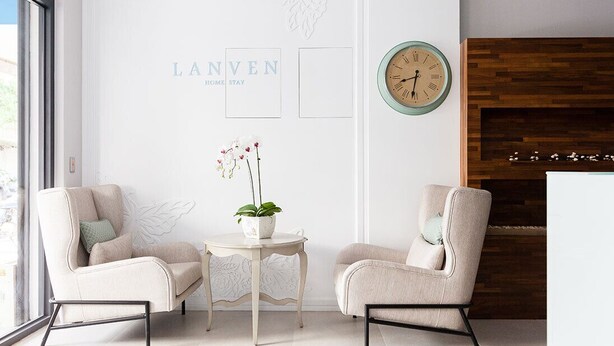A modern room with two armchairs, a small table with a potted orchid, a clock, and a wooden wall panel. - Lanven Art House (Hualien City)