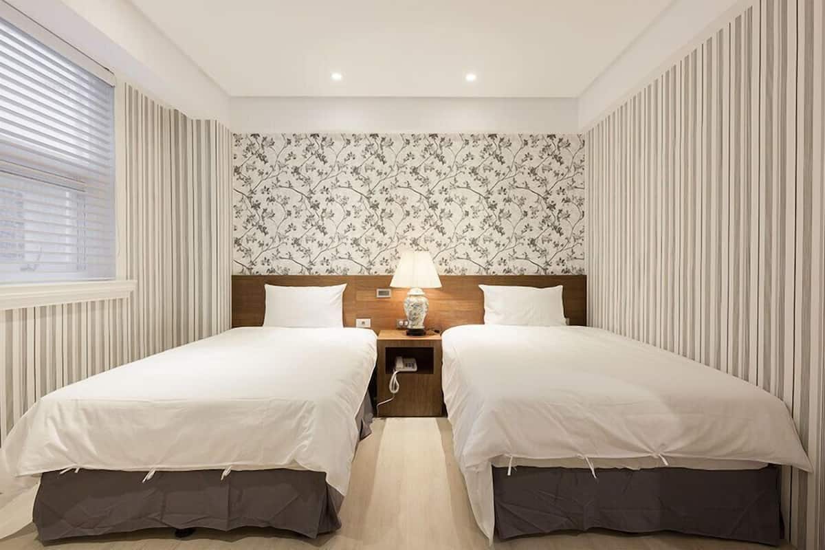A double room with two beds, a nightstand with a lamp, and a floral wallpaper.