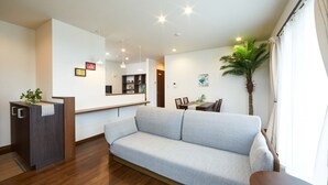 Una sala de estar moderna con un sofá gris, suelo de madera, un pequeño comedor y una recepción.