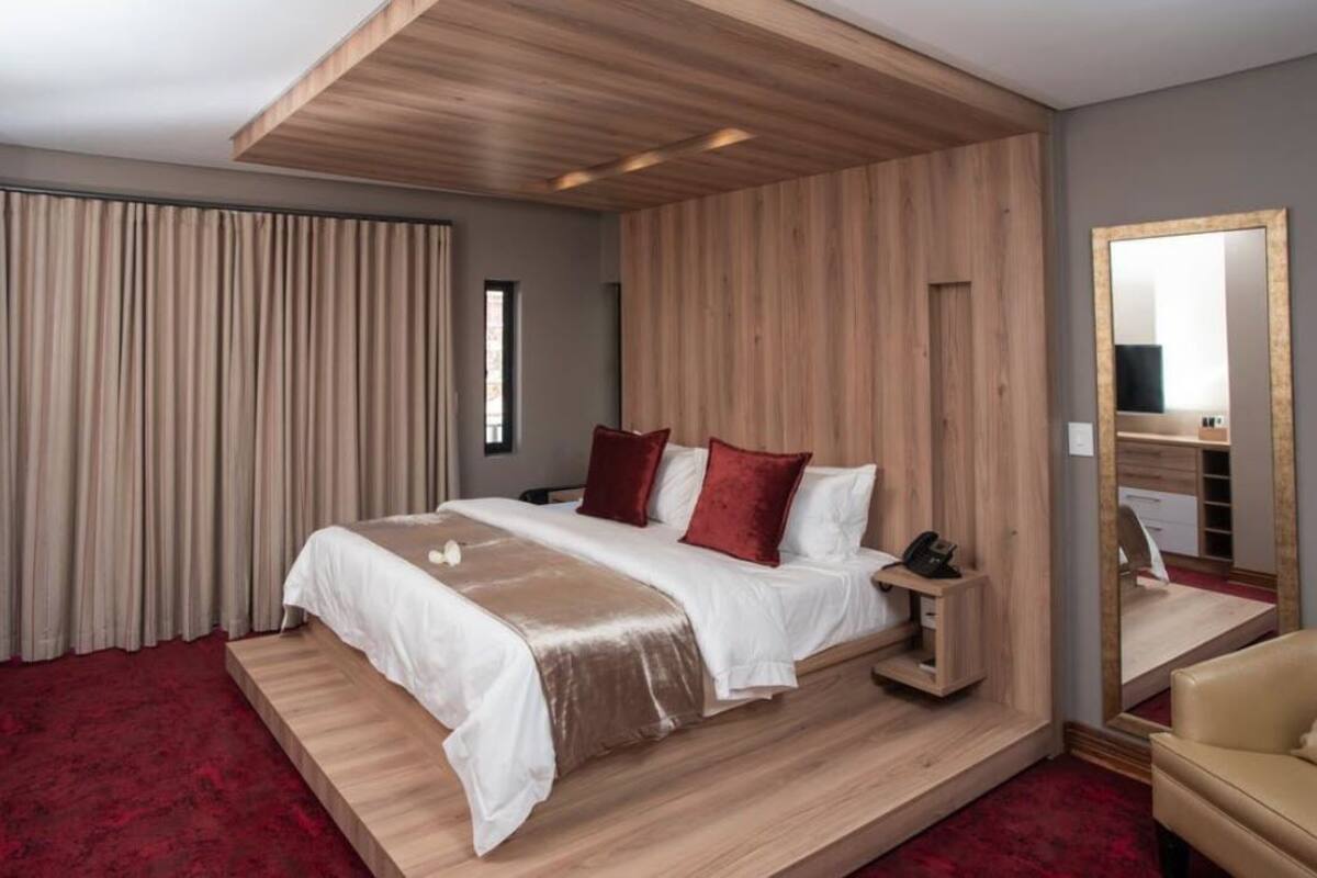 Ein modernes Hotelzimmer mit einem großen Bett, Holzvertäfelung, einem roten Teppich und einem Spiegel.