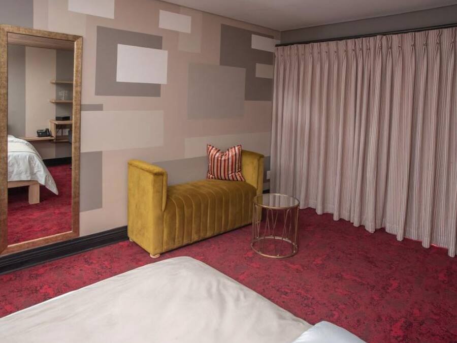 A hotel room with a bed, a yellow armchair, a mirror, a small table, and a curtain.