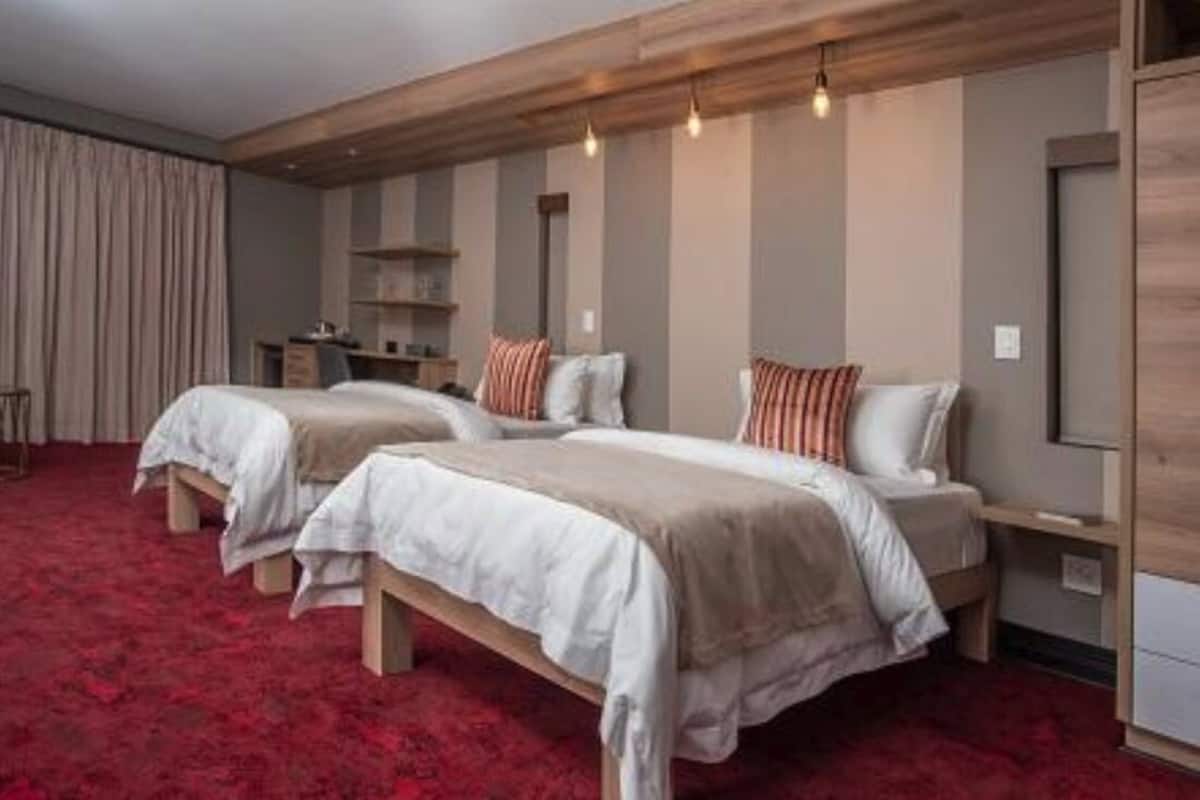 Ein Hotelzimmer mit zwei Betten, einem roten Teppich, einem Holz-Kopfteil und eingebauten Regalen.