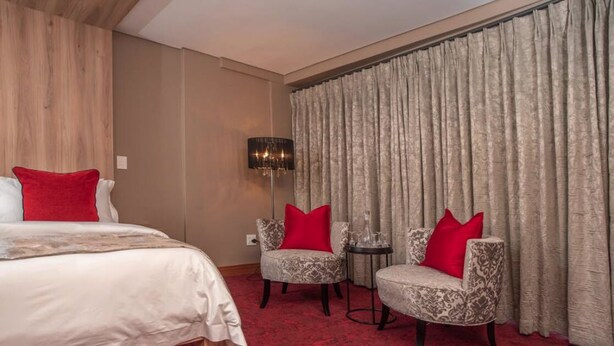A hotel room with a bed, two armchairs, a small table, and a lamp. - Loch Logan Hotel (Bloemfontein)