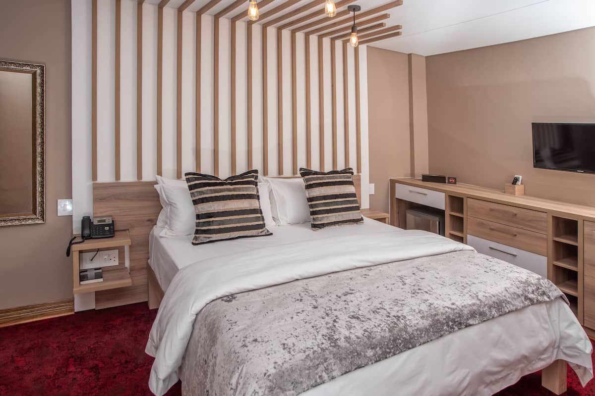 Ein modernes Hotelzimmer mit einem großen Bett, einem Holzkopfschild, Nachttischen, einem Schreibtisch und einem Flachbildfernseher.