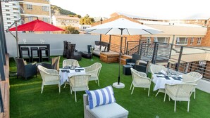 An outdoor patio with wicker furniture, a red umbrella, and a white umbrella. - Loch Logan Hotel (Bloemfontein)