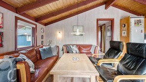 Ein gemütliches Zimmer mit Holzbalkendecke, einer Couch, einem Tisch und Ledersesseln.