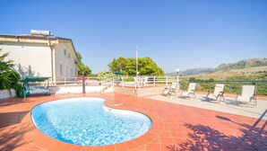 Una piscina al terrat amb vistes a muntanyes, envoltada de gandules i una tanca blanca.