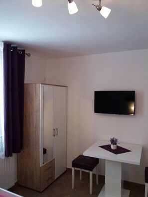 A modern room with a wooden wardrobe, a small table with a chair, and a mounted TV. - Guest House Macic (Plitvicka Jezera)