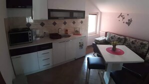 A compact kitchen with a microwave, sink, and a dining area with a table and chairs. - Guest House Macic (Plitvicka Jezera)
