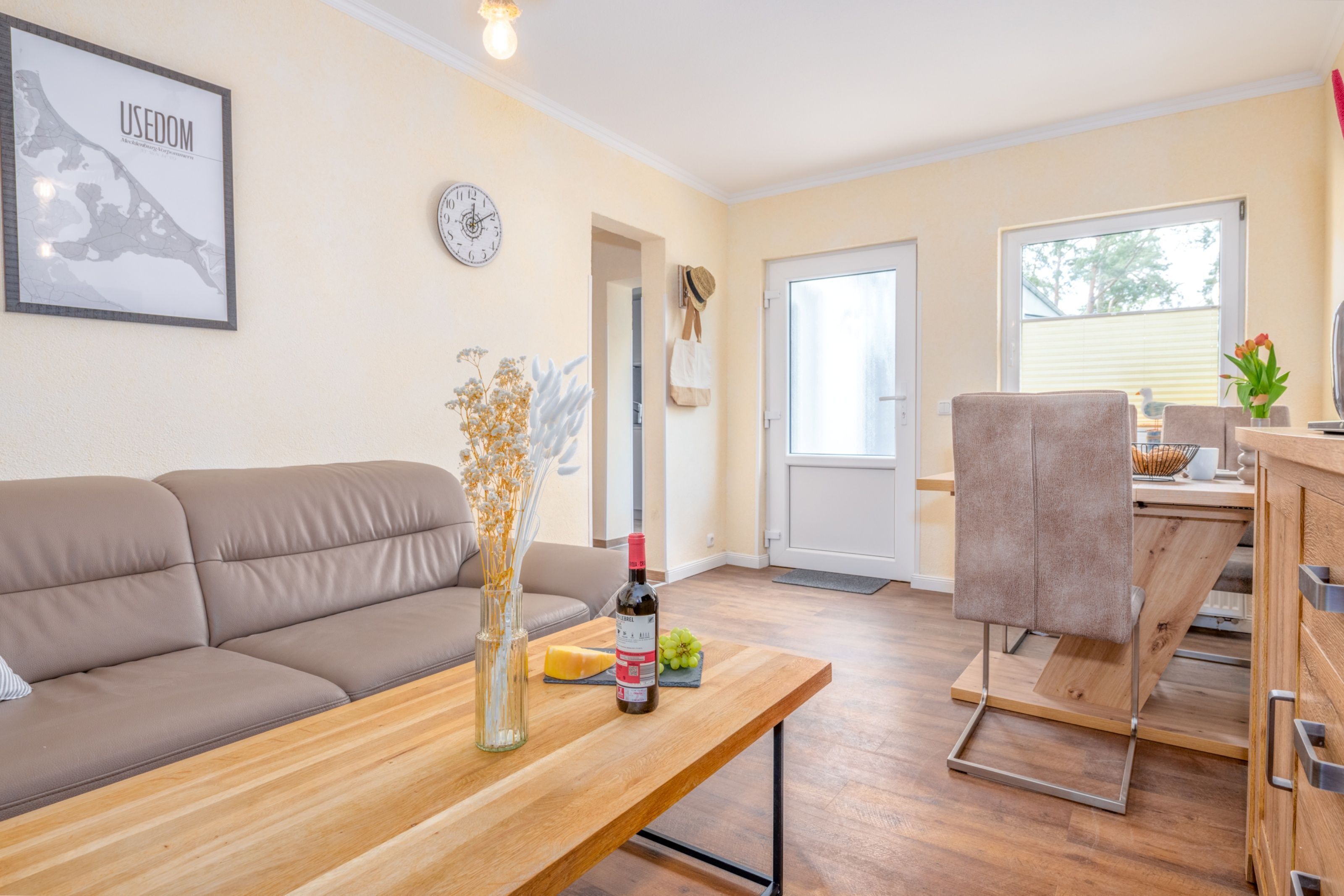 Una sala de estar moderna con un sofá, una mesa de madera con una botella y uvas, y vistas al exterior.