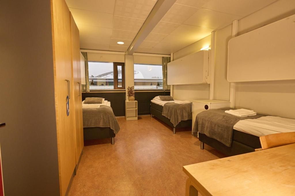 Habitación compacta con tres camas, una mesa de madera y un ventanal con vistas a un edificio.