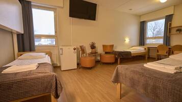 A hotel room with two beds, a television, a refrigerator, and a window with curtains.