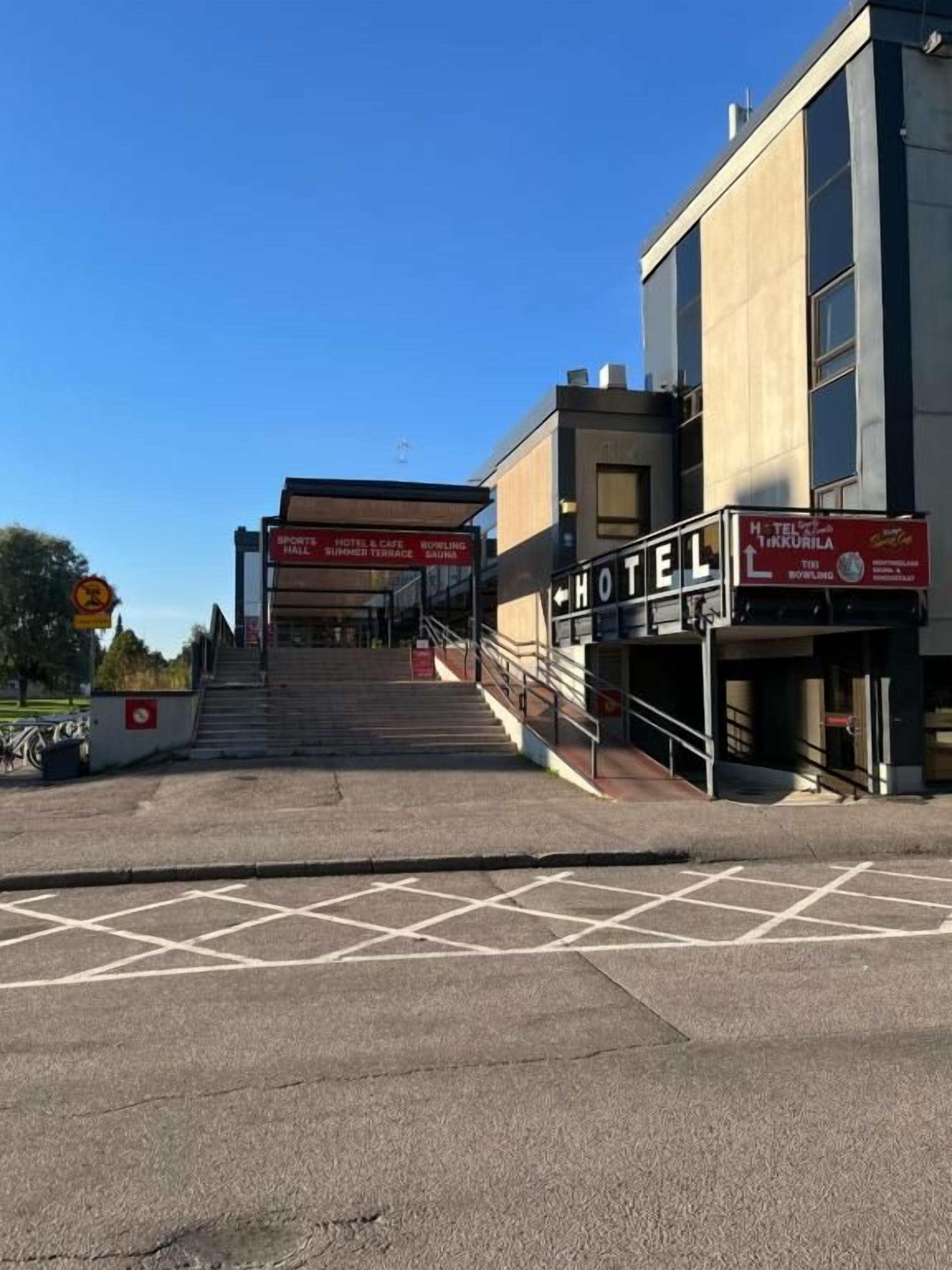 Entrada de un hotel con una escalera que conduce a la recepción, un cartel con el nombre del hotel y un cielo despejado.