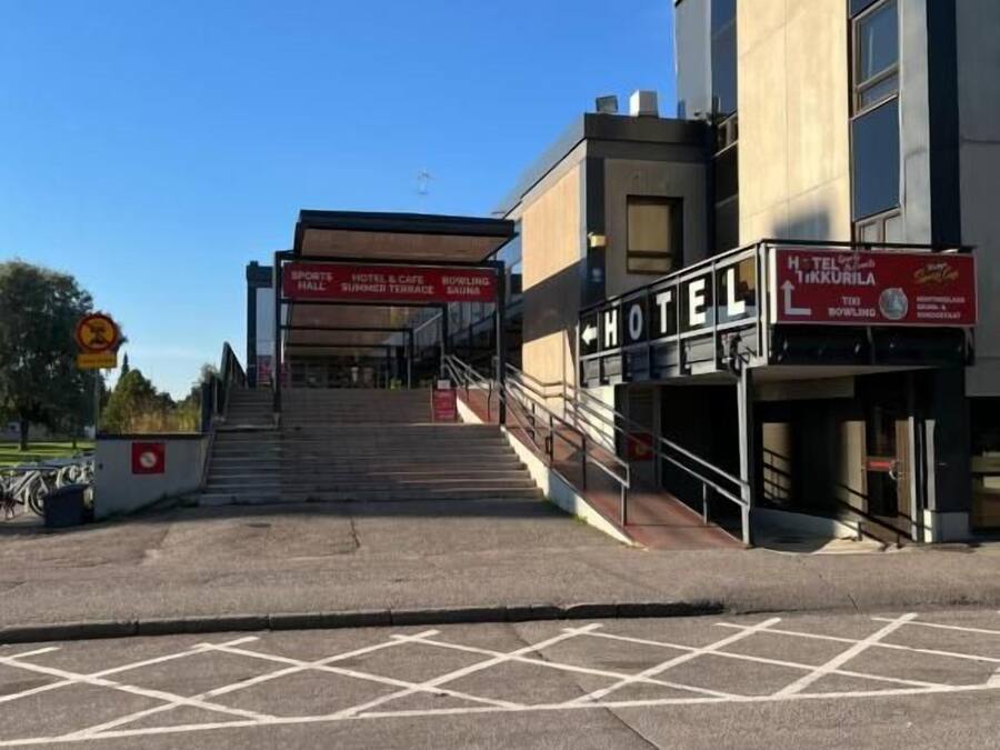 Entrada de un hotel con una escalera que conduce a la recepción, un cartel con el nombre del hotel y un cielo despejado.