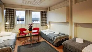 Habitación de hotel con dos camas individuales, una mesita pequeña y dos sillas rojas.