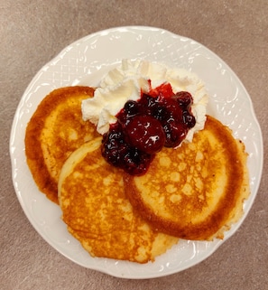 Un plato con tortitas, crema batida y compota de frutos rojos.