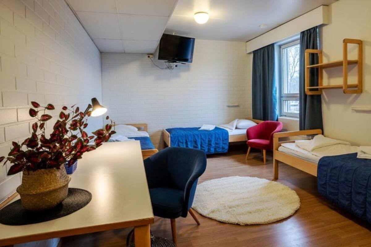 A hotel room with two single beds, a desk with a chair, a TV mounted on the wall, and a window with curtains.