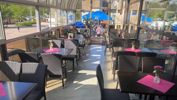 Un espacio de comedor al aire libre con mesas y sillas de metal negro, dispuestas en filas con individuales rosas.