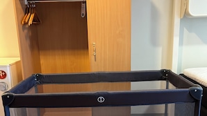Un corralito para bebés con cubierta de malla y un cojín en el interior, sobre un piso alfombrado.