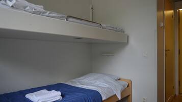 A single-bed room with a bunk bed above, a blue bedspread, and a white towel on the lower bed.