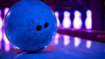 Una bola de boliche sobre una pista de madera con bolos numerados al fondo.