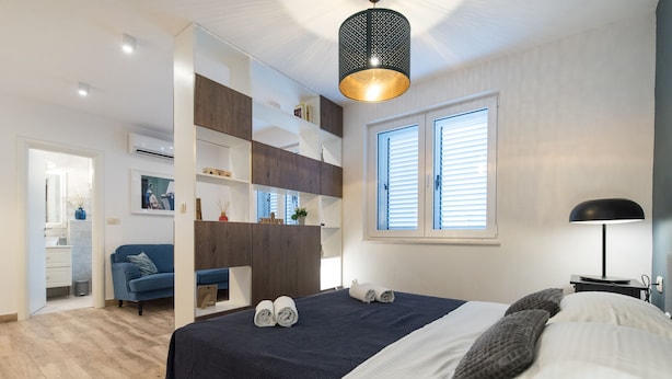 A modern bedroom with a large bed, a wardrobe, a desk, and a window with blinds. - Apartments Cingulice (Kastela)