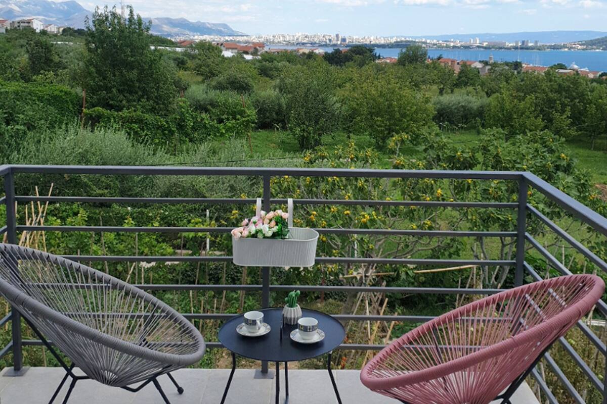 A balcony with two chairs and a small table, overlooking a cityscape and a body of water.