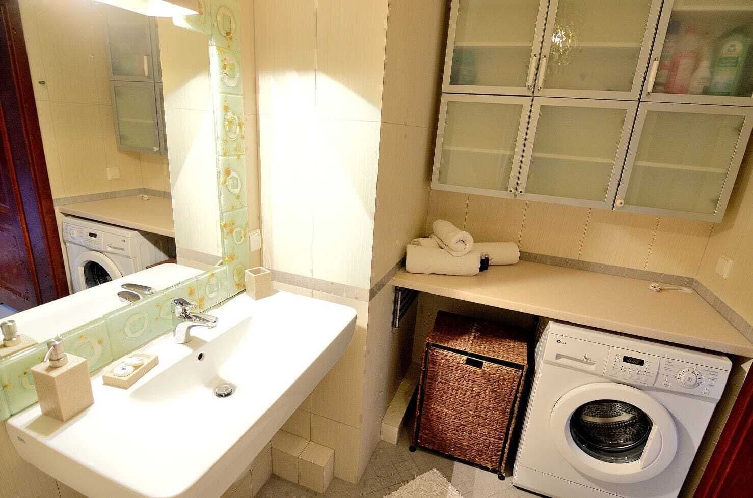 A compact bathroom with a sink, mirror, and a washing machine.