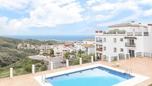 Un edificio residencial con piscina, fachada blanca y vista al mar.