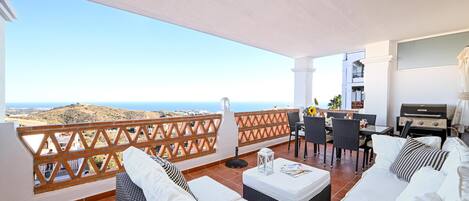 A balcony with a white sofa, a dining table with chairs, and a grill.