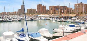 A marina with numerous boats docked, a clear sky, and buildings in the background.