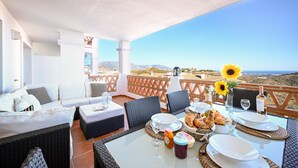 Una terraza con un sofá blanco, sillas de mimbre, una mesa de comedor con platos, vasos y un jarrón de girasoles.