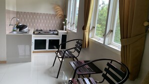 A kitchen with a sink, stove, and two chairs. There are windows with curtains and a view of greenery outside. - Green Homestay (Batu)