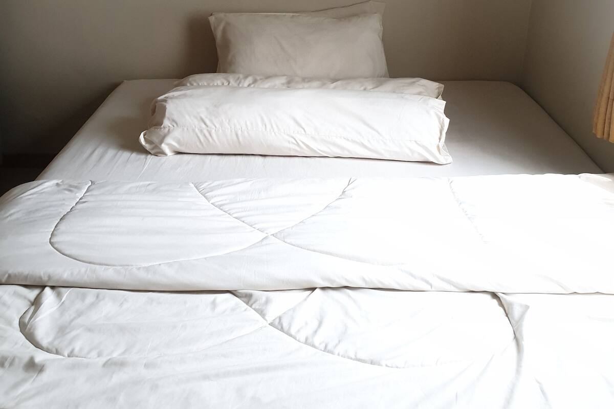 Ein Einzelbett mit weißer Bettwäsche in einem Raum mit schlichten Wänden.