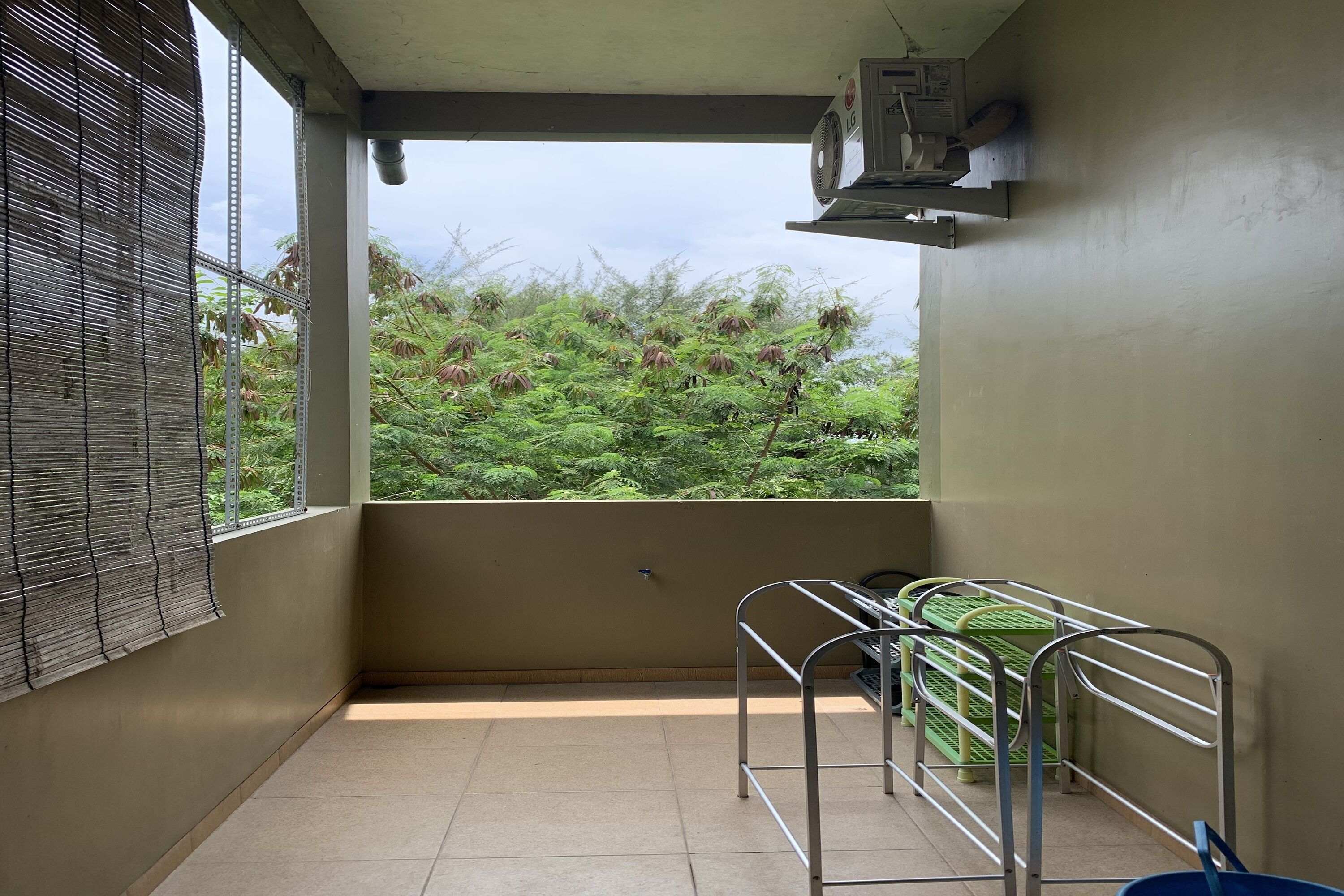 A balcony with a view of greenery, a metal rack, and an air conditioning unit.