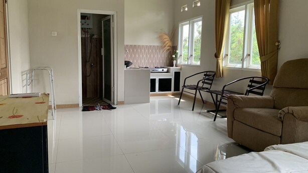 A spacious living area with a sofa, chairs, a small table, and a kitchen area in the background. - Green Homestay (Batu)