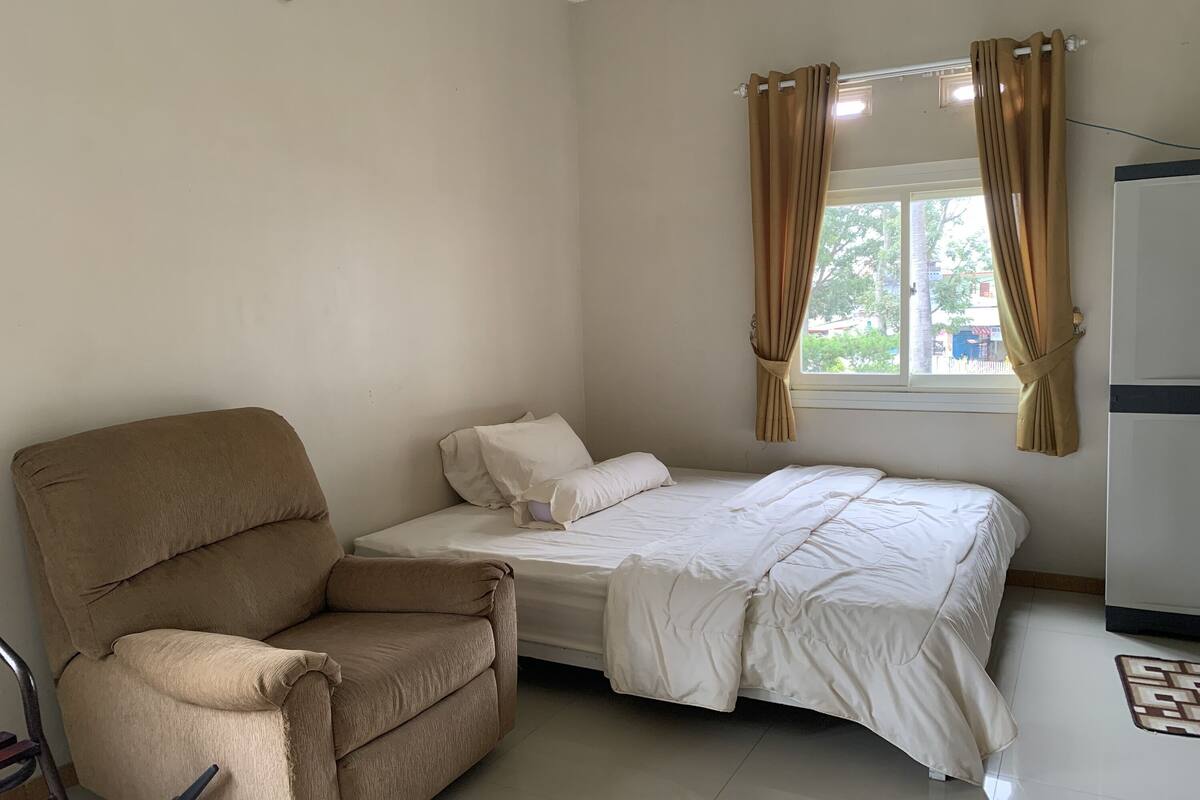 Ein Schlafzimmer mit einem Einzelbett, einem beigefarbenen Sessel und einem Fenster mit Vorhängen.