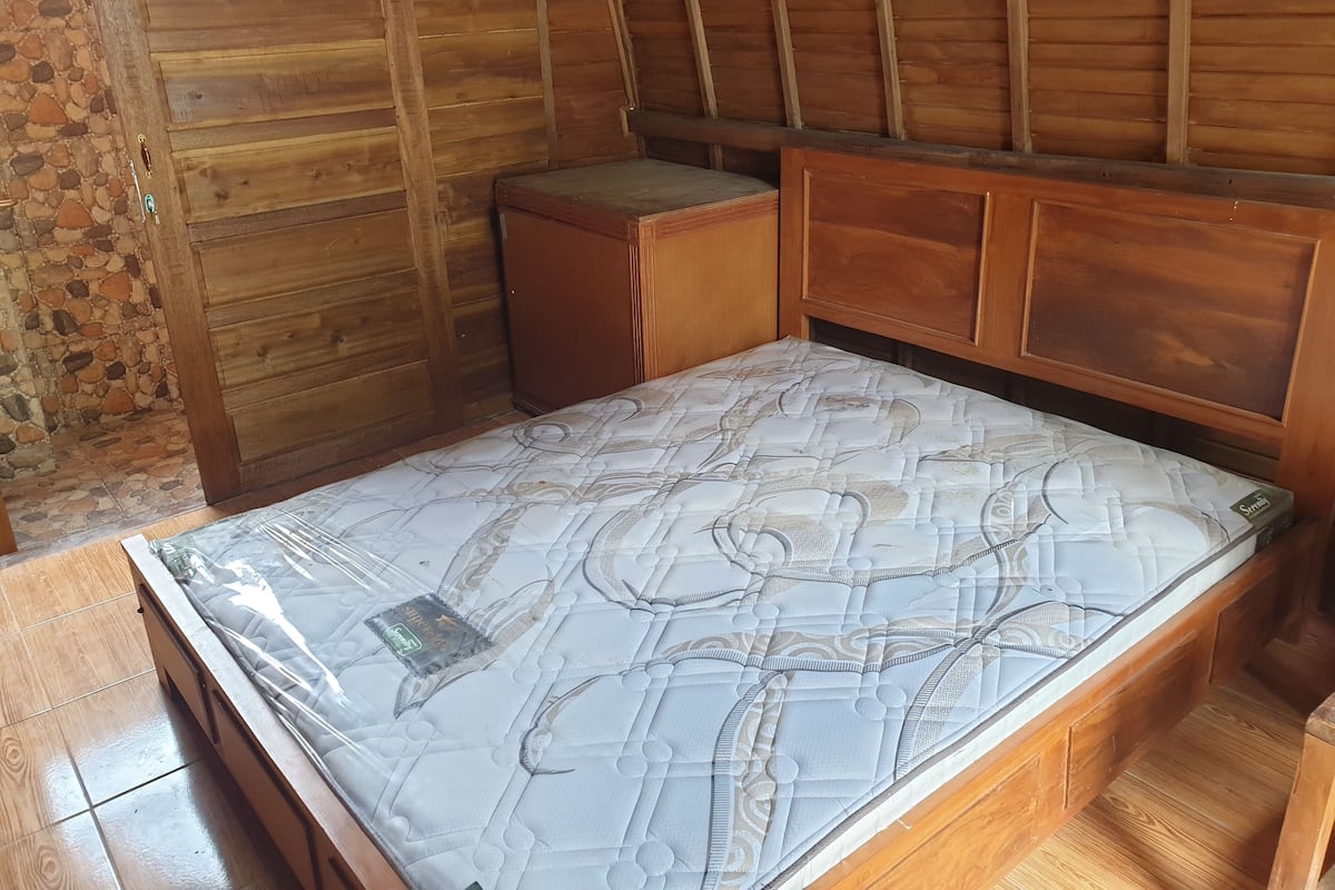Una habitación de madera con una cama, un pequeño armario de madera y una pared de piedra.