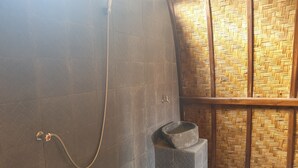 Un baño con ducha, lavamanos de piedra y separador de bambú tejido.