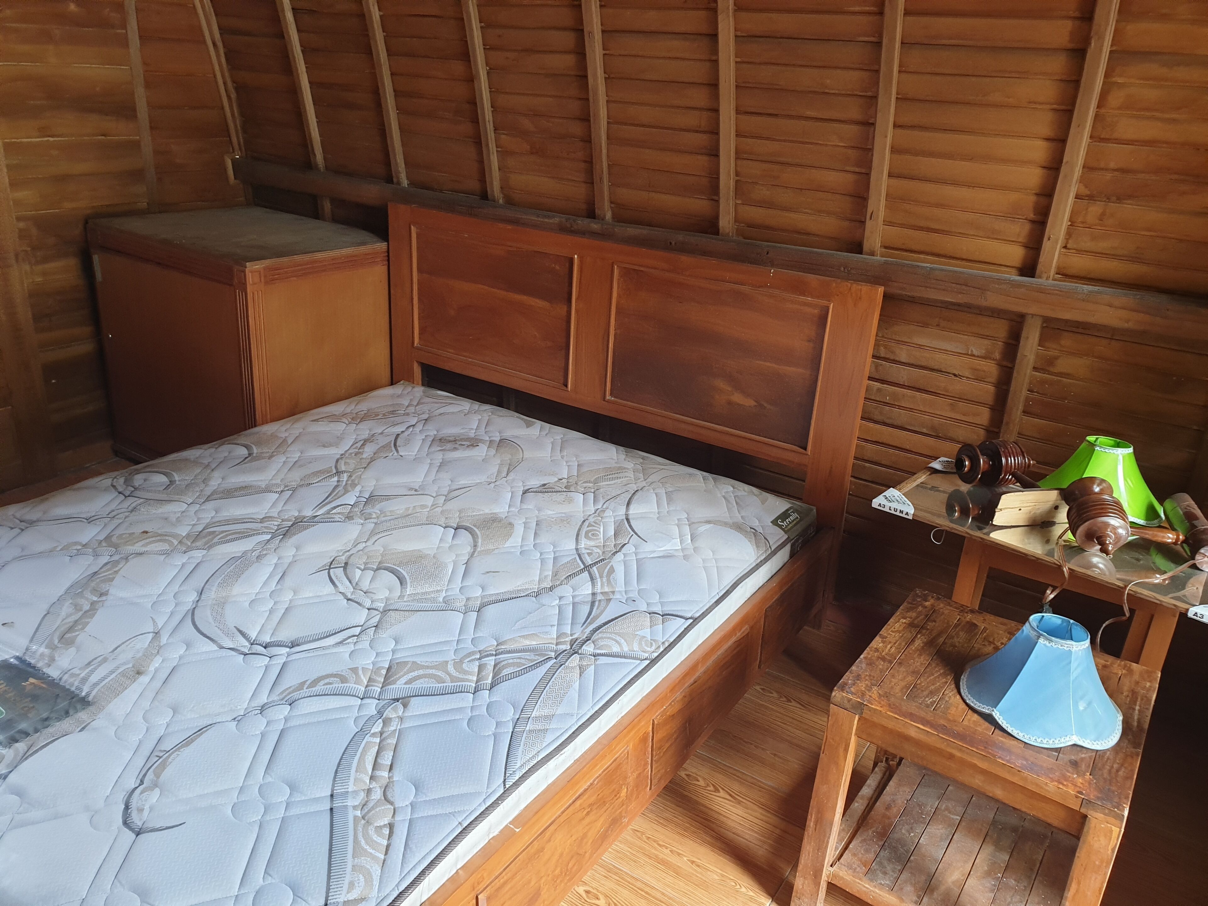 Una habitación de madera con una cama, una mesita con una lámpara y una lámpara verde sobre una mesa de madera.