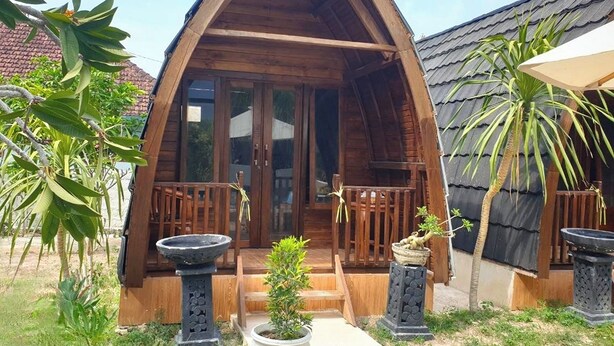 Una cabaña de madera con techo triangular, un porche con barandillas de madera y plantas en macetas.