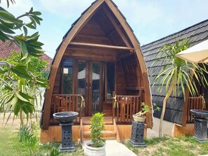 A wooden cabin with a triangular roof, a porch with wooden railings, and potted plants. - Jambu Guesthouse (Penida Island)