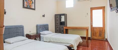 A room with two beds, a wooden door, a small table, a cabinet, and a television on the wall.