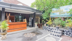 A hotel entrance with a reception desk, outdoor seating, and potted plants. - Mahendra Beach Inn (Kuta)