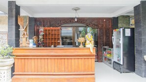 A reception area with a wooden counter, a refrigerator, and a glass door leading to the interior. - Mahendra Beach Inn (Kuta)