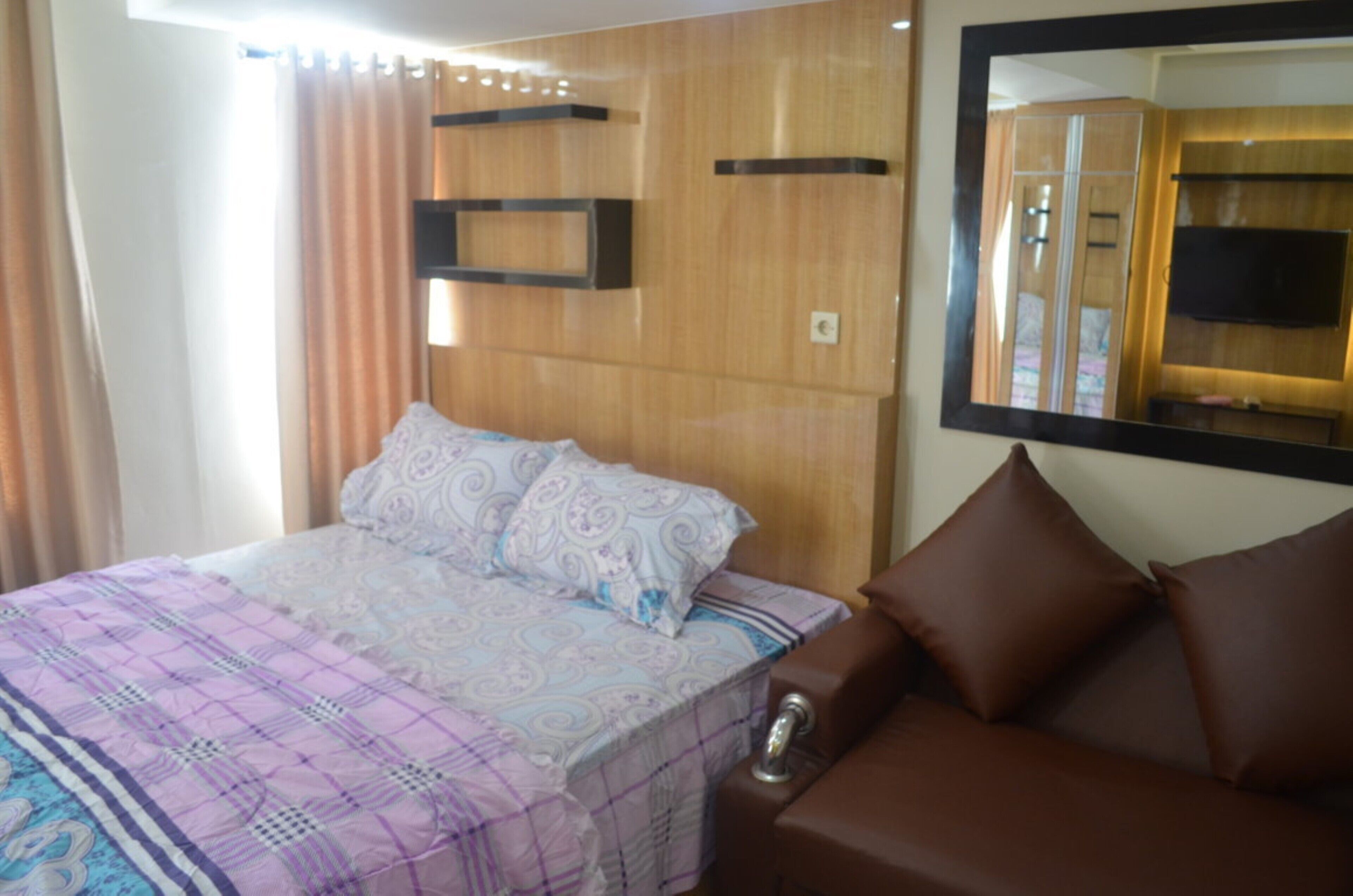 A bedroom with a bed, a brown sofa, a wooden headboard, a mirror, and a wardrobe.