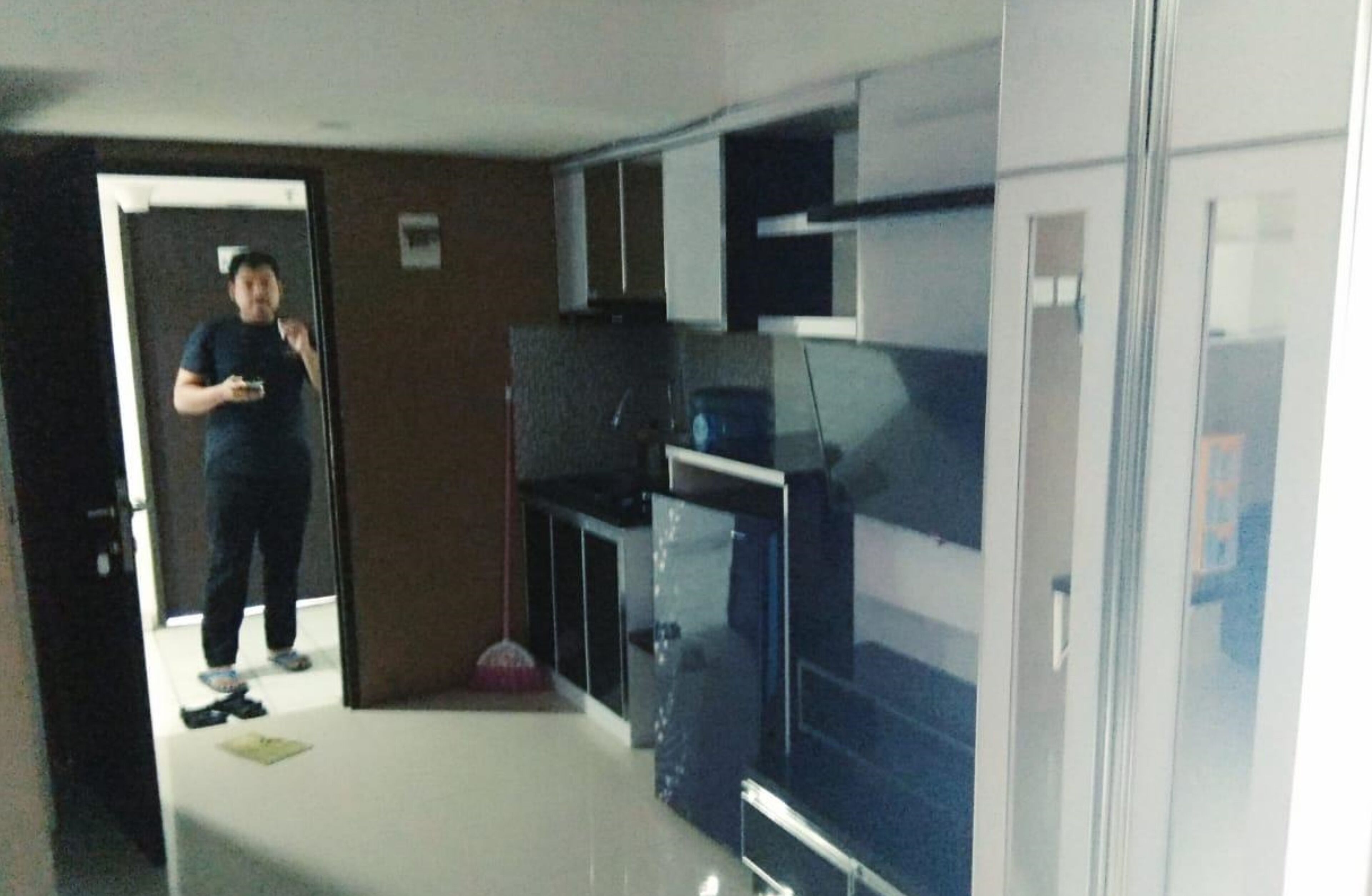 A room with a kitchen area, a door leading to another room, and a mirror reflecting part of the room.