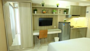 A compact hotel room with a bed, a desk with a chair, a television, a refrigerator, and a small kitchenette.