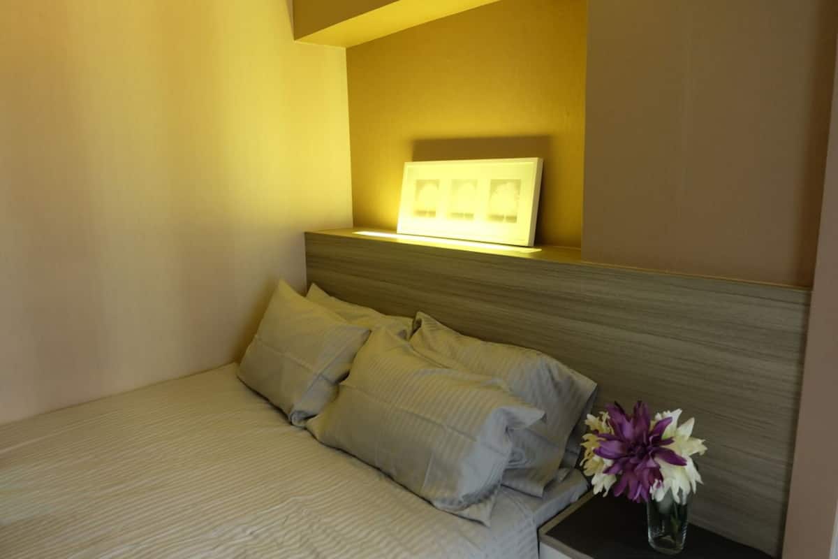 A neatly made bed with pillows, a bedside table with a vase of flowers, and a wall-mounted light fixture.